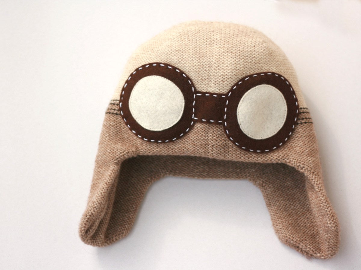 berretto da aviatore fatto a maglia di colore beige chiaro e scuro con gli occhiali marroni in feltro